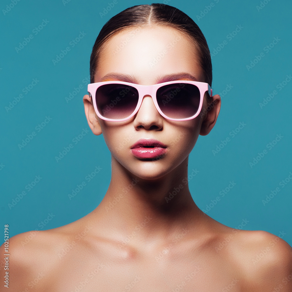 Portrait of beautiful young girl in sunglasses in studio on a blue background Portrait of beautiful young girl in sunglasses in studio on a blue background
