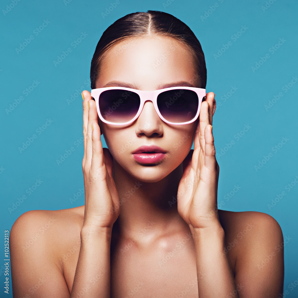 Portrait of beautiful young girl in sunglasses in studio on a blue background Portrait of beautiful young girl in sunglasses in studio on a blue background