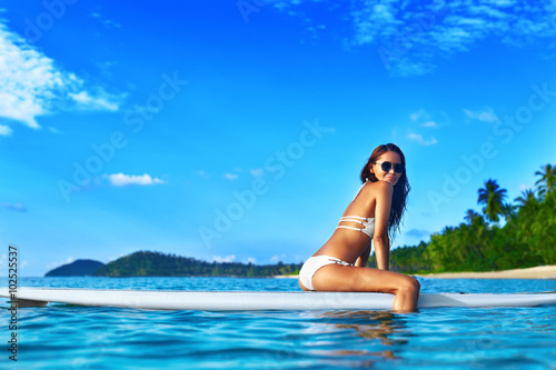 Travel Vacation. Beautiful Sexy Young Woman With Fit Body In White Bikini Relaxing On Stand Up Paddle   Surfing   Board In Sea Water On Tropical Resort. Healthy Lifestyle Concept. Summer Fun. Sports