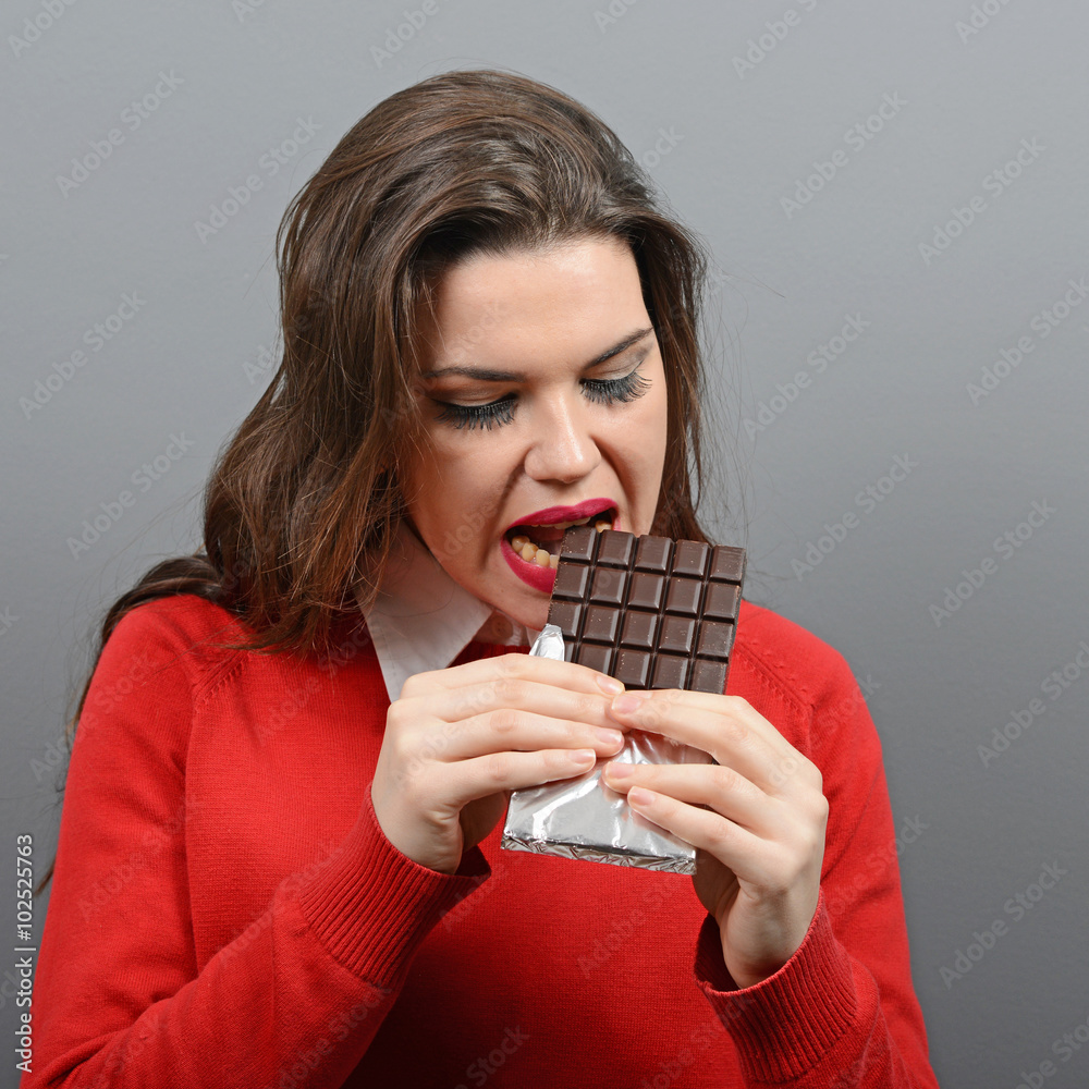 Beautiful woman eating chocolate against gray background Beautiful woman eating chocolate against gray background