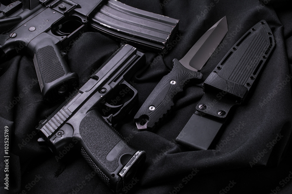 Gun, knife and rifle.Top view/Pistol, rifle and knife with sheath on black fabric. Gun, knife and rifle.Top view/Pistol, rifle and knife with sheath on black fabric.