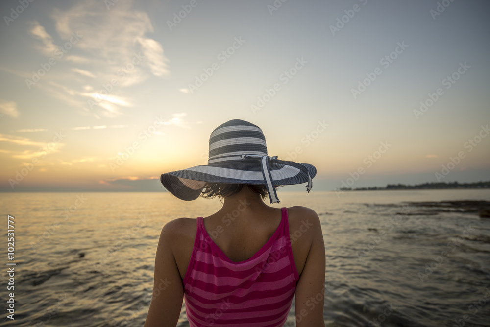 Woman with striped straw hat sitting on the shore looking at the