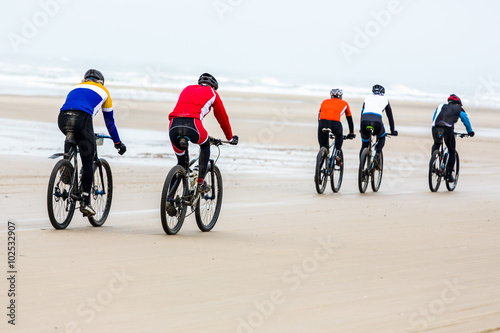 five unrecognizable people drive with mountain bikes on a beach during a contest. 