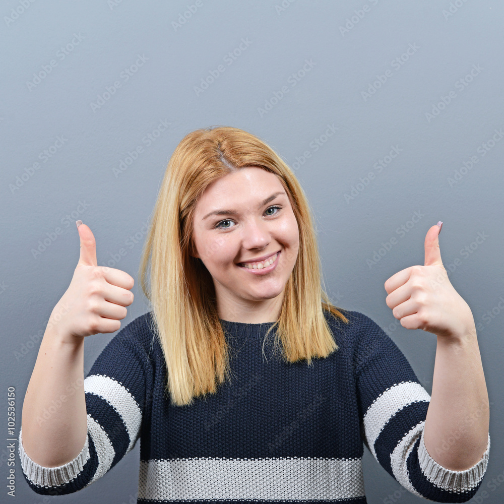 Portrait of happy woman holding thumbs up against gray backgroun Portrait of happy woman holding thumbs up against gray backgroun