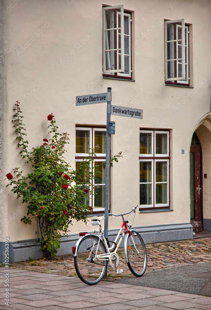 Old building and a white bicycle resting on a lamp post in Lubeck, Germany