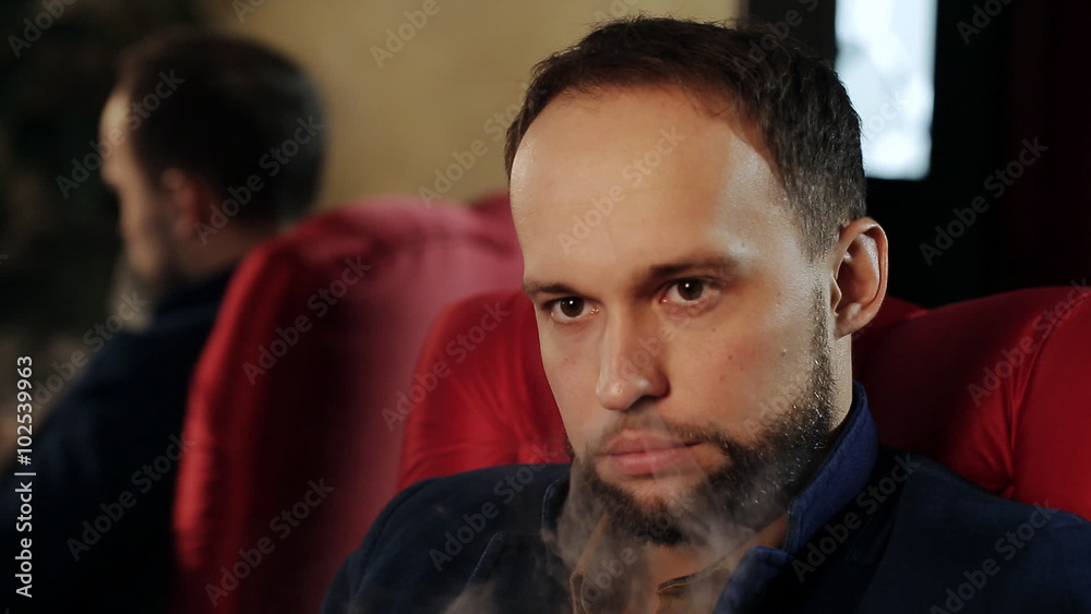 brutal guy with a beard smokes an electronic cigarette in a red armchair brutal guy with a beard smokes an electronic cigarette in a red armchair