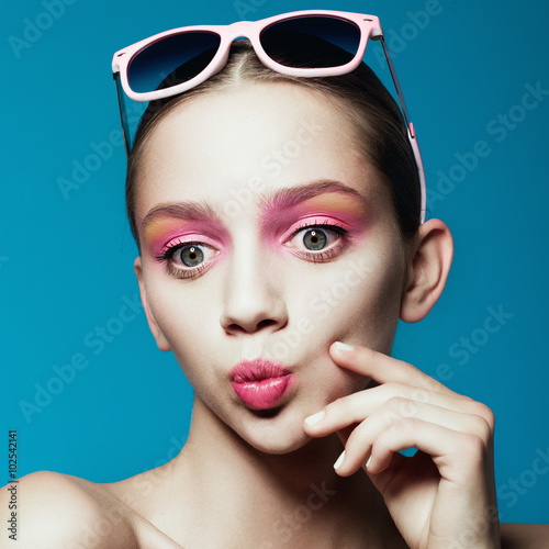 Portrait of beautiful young girl in sunglasses in studio on a blue background