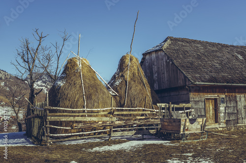 Spring rural scene with traditional Romanian farm with wooden barn, haystacks and large sleigh in Magura village, Brasov county, Transylvania region, Romania.