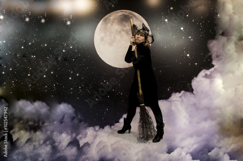 Девушка в черной одежде, изображающая ведьму, на фоне облаков и луны