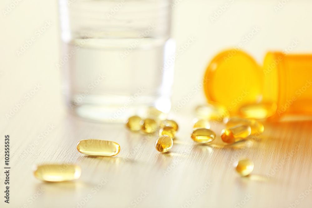 Yellow capsules spilled from pill bottle and glass of water on the table, close up Yellow capsules spilled from pill bottle and glass of water on the table, close up
