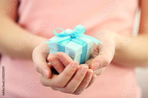 Female hands holding beautiful small gift wrapped with satin ribbon. © Africa Studio