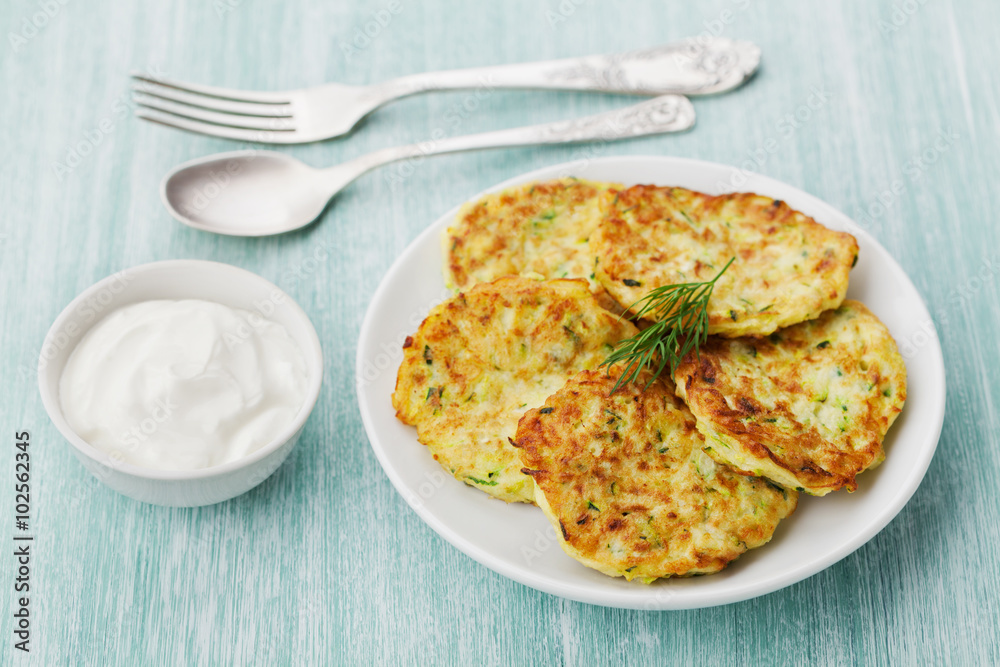 Vegetable zucchini cabbage pancakes or fritters with sour cream on wooden kitchen table