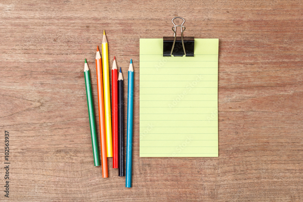 Green lined note paper with color pencils on wood table for back Green lined note paper with color pencils on wood table for back