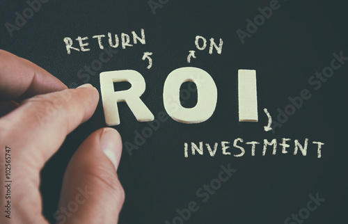 man hand pointing at the words ROI Return On Investment written on black leather background
