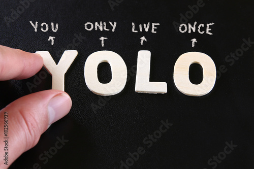 man hand pointing at the words YOLO you only live once written on  black leather background photo