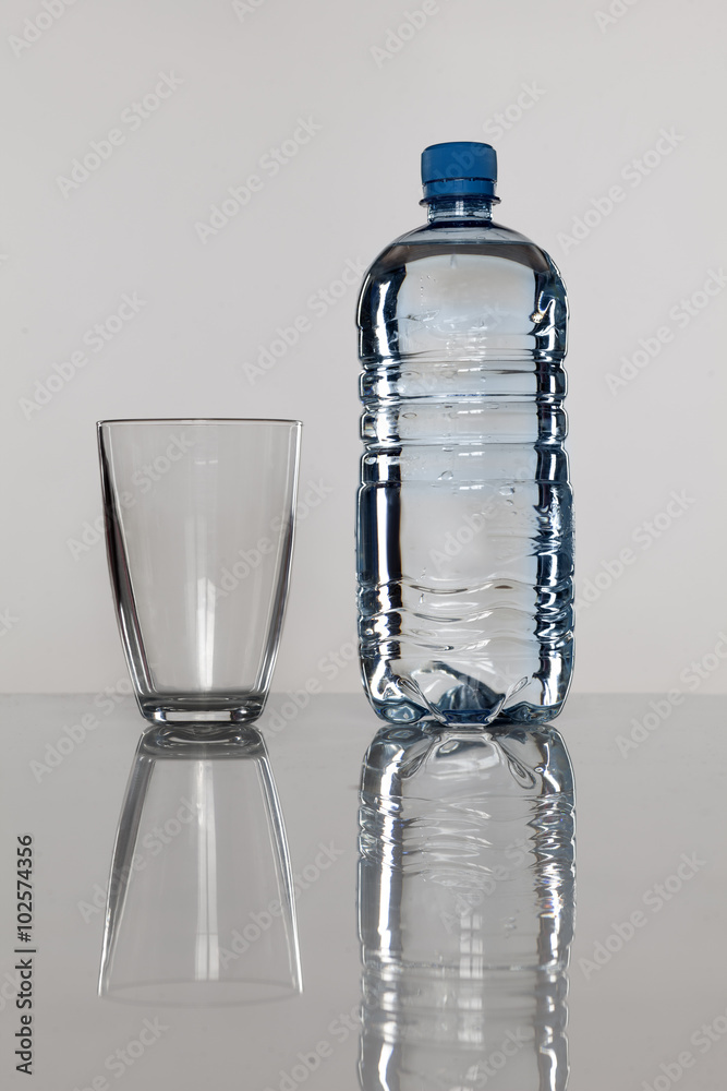 plastic bottle with water and empty glass next to bottle plastic bottle with water and empty glass next to bottle