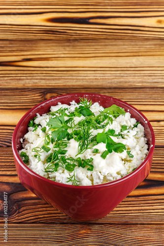 Fresh cottage cheese with sour cream, dill, parsley, onion in ceramic bowl on wooden table, space for text