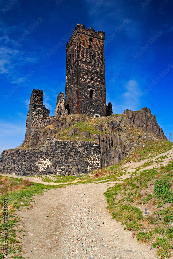 Hazmburk gothic castle on rocky mountain, with gravel path and blue sky, in Ceske Stredohori, Czech republic.