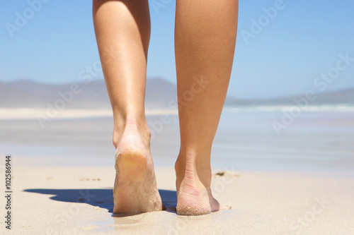 Woman walking barefoot on beach from behind