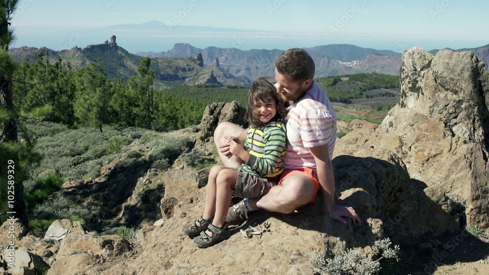 Father sitting with his son on the rock and smiling to the camera
Father sitting with his son on the rock and smiling to the camera