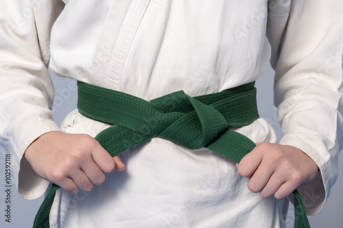 Hands tightening green belt on a teenage dressed in kimono for martial arts. Sepia toning