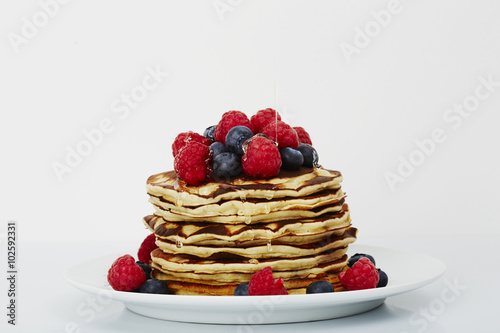 Pancakes topped with fruit and honey in white studio