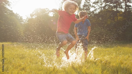 Two kids jumping in puddle splashing water