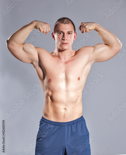 Young muscular  man showing his biceps on gray background