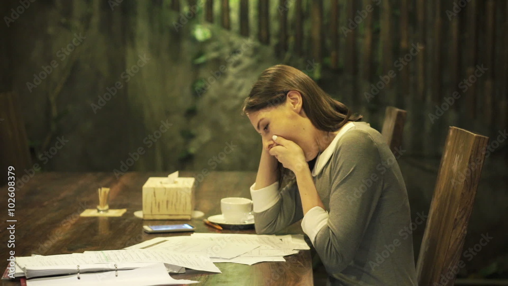 Young, sleepy businesswoman with documents sitting by table at home at night 
