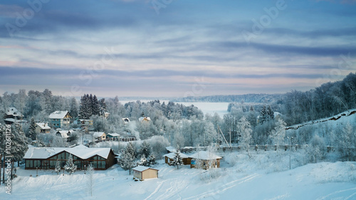 Snowy forest and cottages and iced lake at sunset