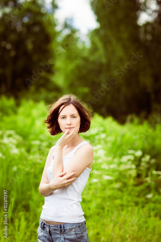 Adorable young woman touching her face wtih her hand in summer forest, field. Femininity and womanhood concept