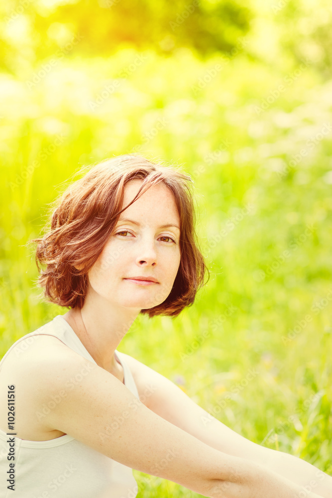 Outdoor portrait of adorable freckled young woman who sitting on green grass in summer park on sunny day . Orange and yellow natural toning. Femininity and womanhood concept Outdoor portrait of adorable freckled young woman who sitting on green grass in summer park on sunny day . Orange and yellow natural toning. Femininity and womanhood concept