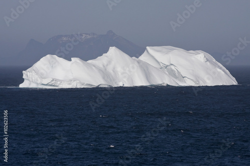 Iceberg Floating in Ocean with Mountains in the Background