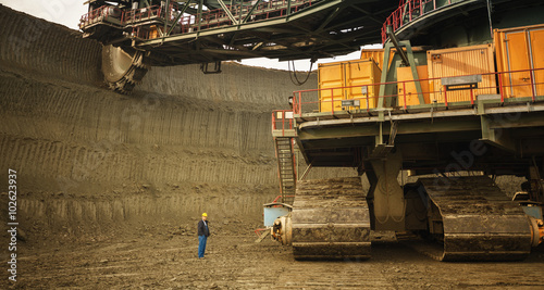 Coal mine worker with a helmet on his head standing in front of huge drill machine and looking at it. photo