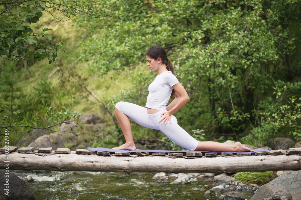 Beautiful young woman meditating in yoga pose at a mountain stream. Selective focus on woman. Beautiful young woman meditating in yoga pose at a mountain stream. Selective focus on woman.