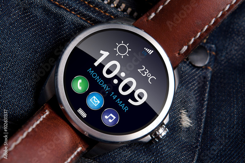 Smart watch concept on matte and polished metal case with brown leather strap on blue jeans background, display turned on