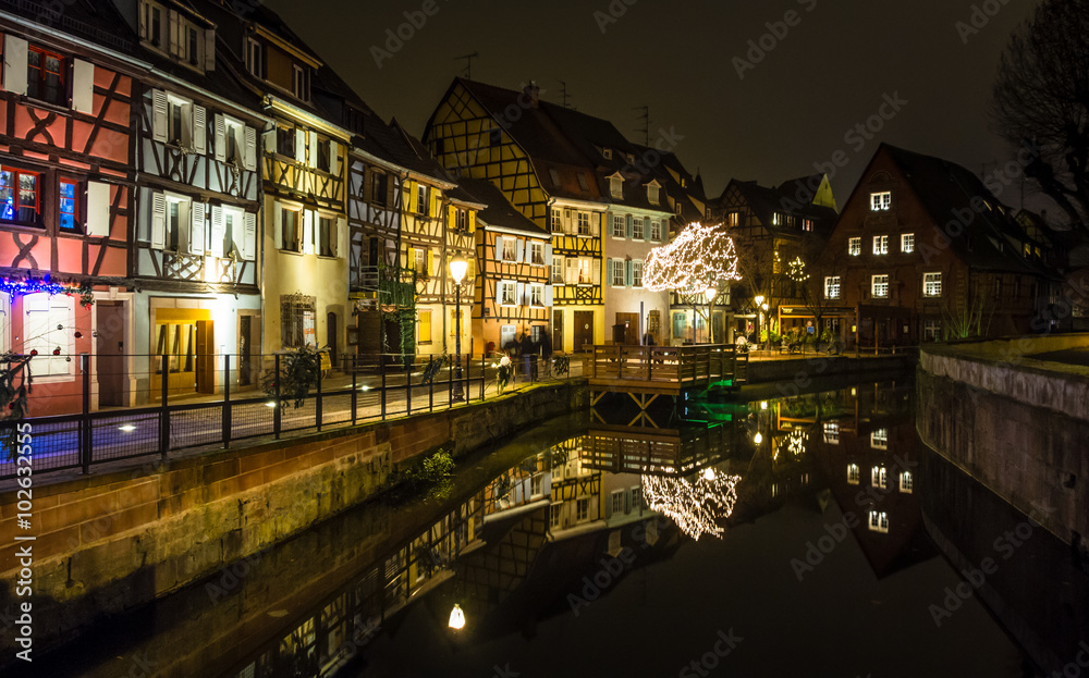 Semi-timbered houses by a canal in Colmar, lit up in the evening during Christmas time