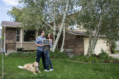 couple and dog in front of new home staring at each other with sold sign