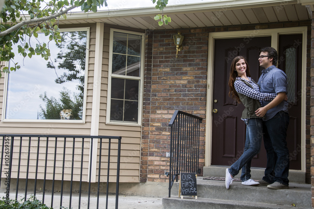 new home owners on front door steps of new home as dog looks out window new home owners on front door steps of new home as dog looks out window