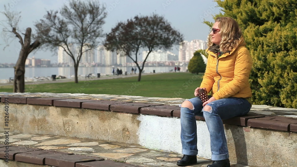 Portrait of a woman sitting in city park and holding a thermos Portrait of a woman sitting in city park and holding a thermos