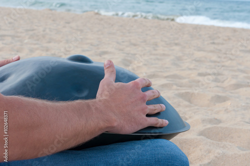 Man on the sand beach playing handpan or hang with sea On Background. The Hang is traditional ethnic drum musical instrument
