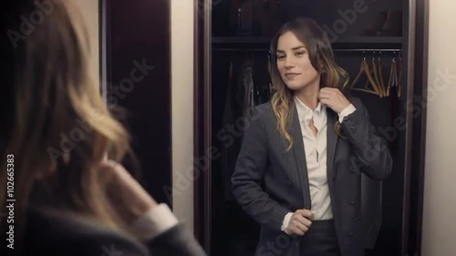 Confident business woman gets ready in front of a mirror, looking at herself happy. She smiles and leaves.
