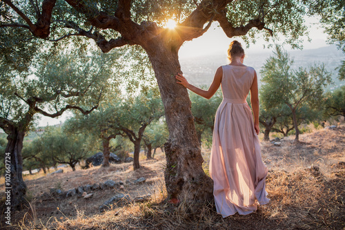 Yong women in olive field looking toward the sea on sunset