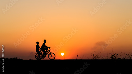 Silhouette of cyclist with friend motion on sunset background