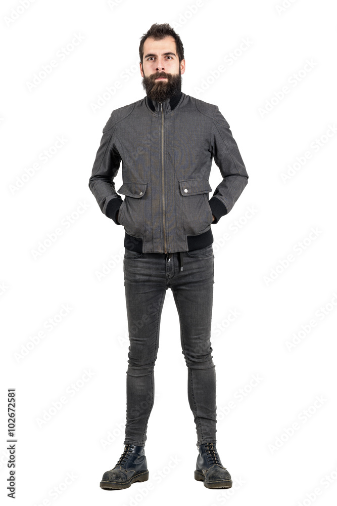 Confident bearded hipster in gray jacket, tight jeans and army boots looking at camera. Full body length portrait isolated over white studio background. Confident bearded hipster in gray jacket, tight jeans and army boots looking at camera. Full body length portrait isolated over white studio background.
