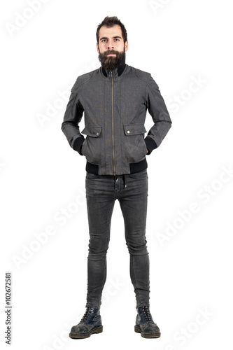 Confident bearded hipster in gray jacket, tight jeans and army boots looking at camera. Full body length portrait isolated over white studio background. 