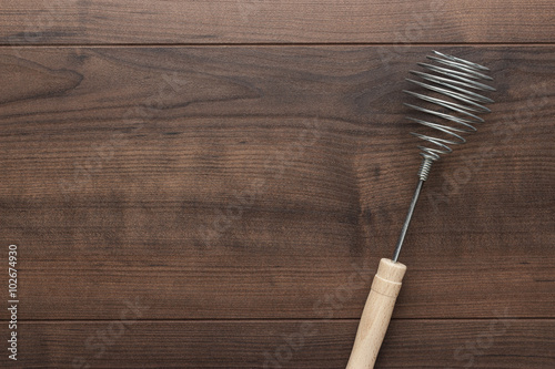 retro egg whisk with wooden handle on brown table with copy space