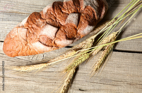 rustic crusty bread and wheat ears on a dark wooden table