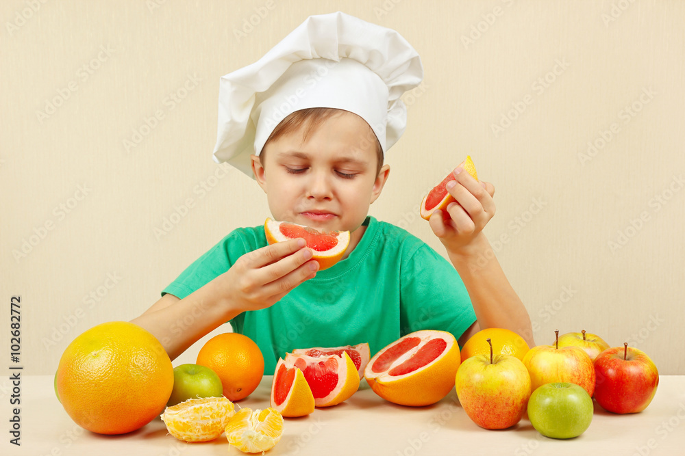 Little funny boy eat fresh grapefruit at the table with fruits Little funny boy eat fresh grapefruit at the table with fruits