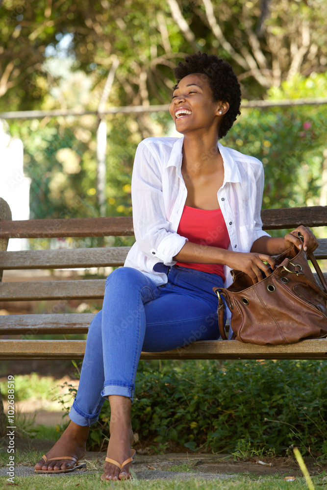 Smiling african woman sitting on a park bench with a bag Smiling african woman sitting on a park bench with a bag
